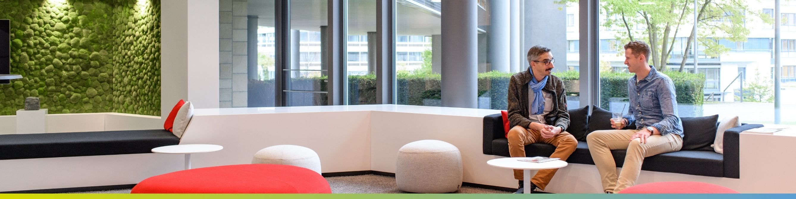 Zwei Kollegen sitzen im Eingangsbereich im Büro und beraten sich zu einem neuen Kundenprojekt