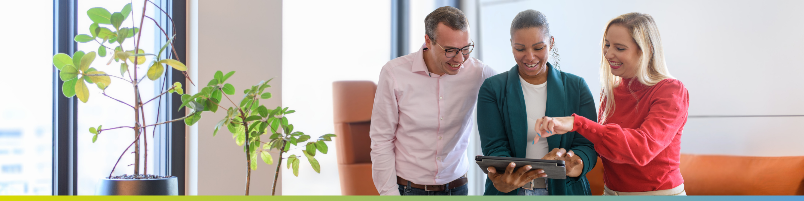 Drei Mitarbeitende stehen in einem modernen Büro und schauen gemeinsam auf ein Tablet.