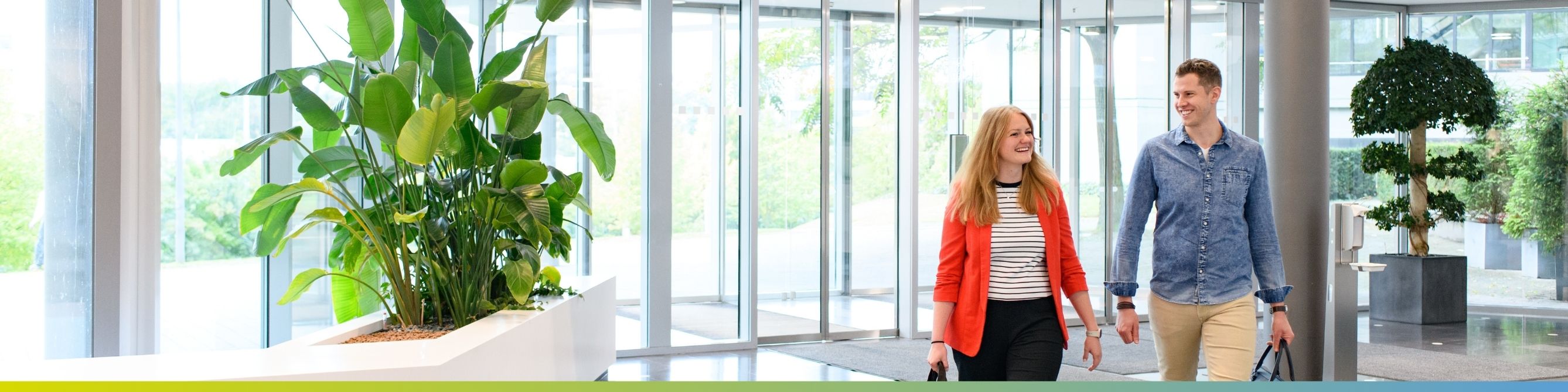 Eine Kollegin und ein Kollege laufen lächelnd durch den Eingangsbereich in unserem Standort in Stuttgart